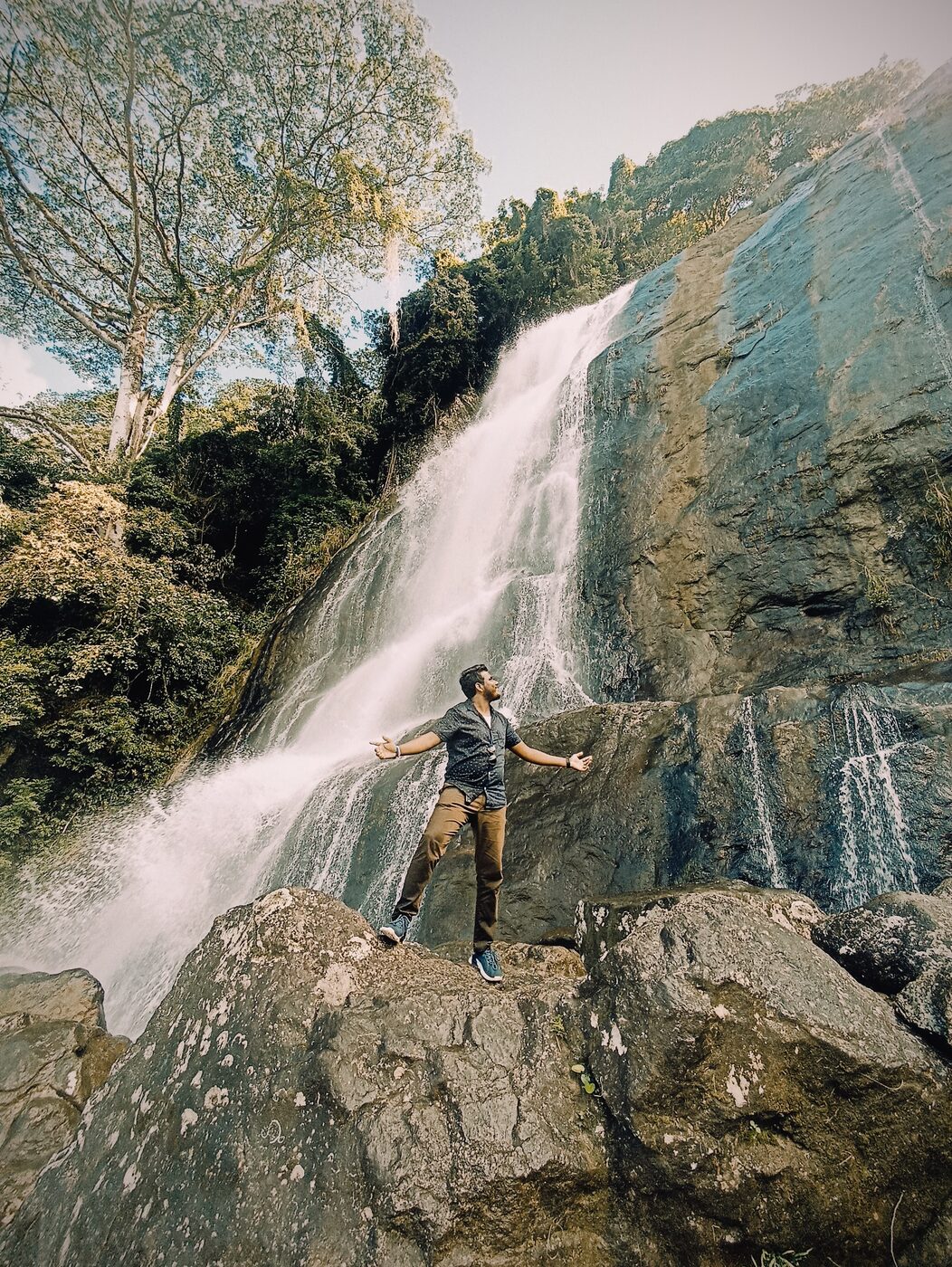 Traveller posing beside a cascading waterfall in the Sri Lankan hills